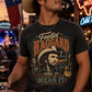 Man wearing a t-shirt with a graphic of a cowboy and text, holding a beer bottle in a lively bar setting.